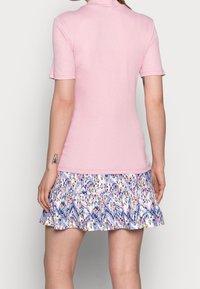 Světle růžový žebrovaný top s krátkými rukávy, zkombinovaný s mnohobarevnou sukní s volány, která má květinové a geometrické vzory.