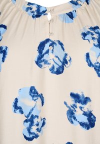 Blouse beige clair avec de grands motifs floraux bleus, présentant un col rond, une ouverture en trou de serrure et quatre boutons sur le devant.