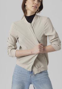 Light beige bomber jacket with a zip closure, ribbed cuffs, and hem. Made of smooth fabric, features a relaxed fit and side pockets.