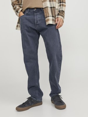 Donkerblauwe, ruime jeans met een rechte pijp, voorzien van een knopenfront, riemlussen en zijzakken, gecombineerd met zwarte sneakers.