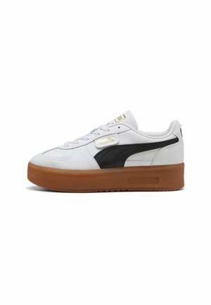 Hvid Puma-sneakers med sort sidestribe og tyk brun sål, lavt design og snørelukning på hvid baggrund.