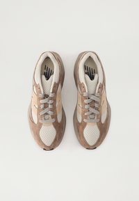 Beige och bruna sneakers med meshtyg och mockadetaljer. Rund tå, vadderad krage och ljusgrå snören. Gummisula med subtil textur.