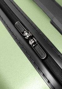 Close-up van een dubbele zwarte rits met "REDOLZ" branding op een gestructureerd lichtgroen kofferoppervlak.