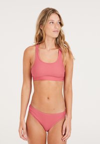 Ružový bikiny top s rebrovaným vzorom, širokými ramienkami a hlbokým výstrihom, v kombinácii s farebne zladenými nízko posadenými bikiny spodkami. Vyrobené z elastického materiálu.
