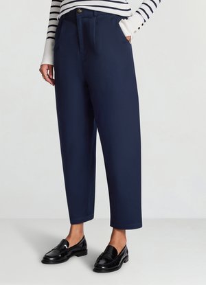Pantalon taille haute bleu marine avec poches latérales, fermeture devant par boutons, et coupe effilée longueur cheville, associé à des mocassins noirs.