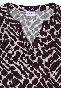 Korte mouwen top in crème met een donkerpaars abstract dierenpatroon, voorzien van een v-hals en een label met de tekst "CECIL." Zachte katoenen textuur.