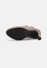 Beige suede women's ankle boot with pointed toe and black sole, viewed from the bottom on a white background.