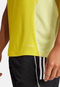 T-shirt de sport jaune avec un panneau latéral en mesh, arborant la marque "AEROREADY". Associé à un short noir avec des rayures blanches.