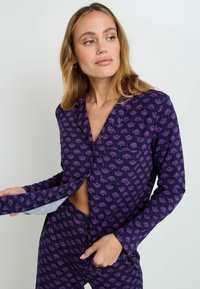 Set di pigiama viola composto da una camicia con bottoni e colletto a punta, decorata con un motivo floreale su tutta la superficie, abbinata a pantaloni coordinati.