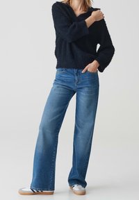 Pull en maille texturée bleu marine associé à un jean large bleu clair et des baskets grises avec des accents blancs.