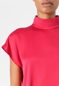 Bright pink short-sleeve blouse with a high neckline, made of smooth, lightweight fabric. Minimalist design with no visible patterns or accents.
