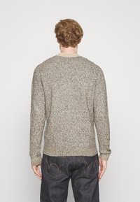 Pull en tricot gris clair avec un col rond, tissu texturé et bordures côtelées aux poignets et à l'ourlet. Porté sur un jean foncé, vu de l'arrière.