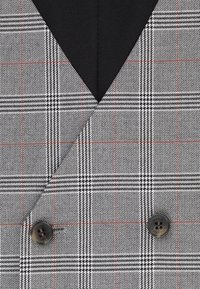 Dwurzędowa marynarka w czarno-szaro-białą kratę, z czarnym klapem i dużymi brązowymi guzikami. Teksturalna tkanina.