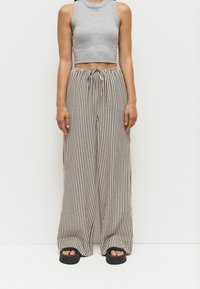 Grå cropped tanktop med ribbet tekstur, parret med bredbenede bukser i sort og hvid strib. Justerbar snor i taljen og flade sandaler.