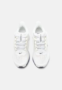 White Nike Pegasus running shoes with mesh upper, round toe, and cushioned sole. Features black Nike logo and textured laces.
