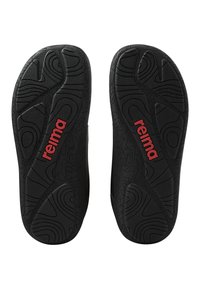 Czarne gumowe podeszwy butów z misternymi wzorami tekstur i wyraźnym czerwonym logo "reima". Wytrzymałe i zaprojektowane z myślą o przyczepności i trakcji.
