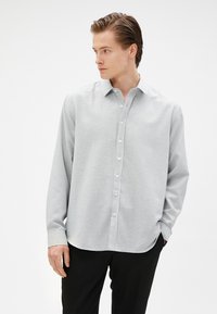 Lichtgrijs button-up shirt met een kraag, lange mouwen en een rechte zoom. Materiaal lijkt glad met een subtiele textuur.