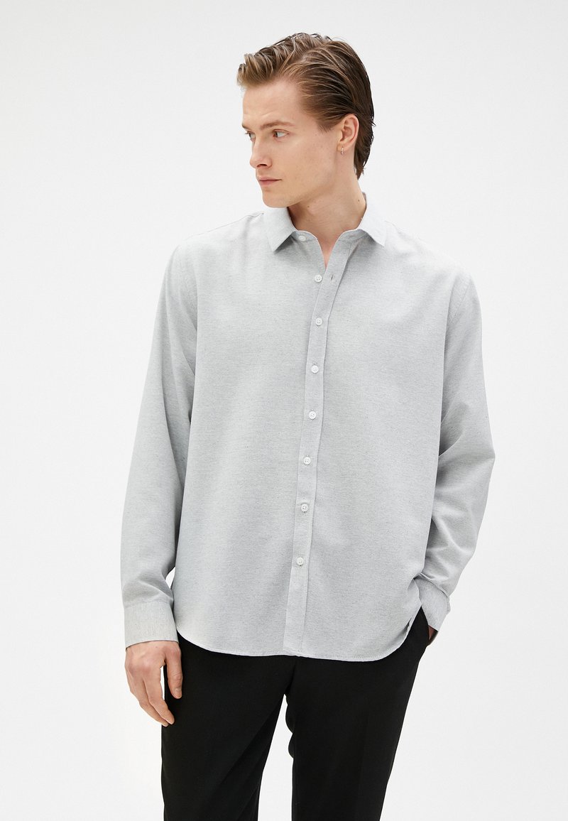 Lichtgrijs button-up shirt met een kraag, lange mouwen en een rechte zoom. Materiaal lijkt glad met een subtiele textuur.