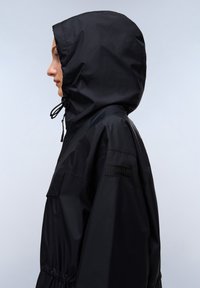 Zwarte hoodie met een glanzende textuur, elastische trekkoord bij de capuchon en een merkaaccent op de mouw. Heeft een relaxte fit met zakken.