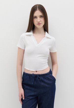 Top bianco corto con tessuto testurizzato, maniche corte e colletto a V, abbinato a pantaloni in denim blu scuro con vita elastica.