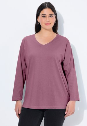 Lange mouw, V-hals top in mauve, heeft een relaxte pasvorm en zachte stof. De mouwen zijn iets taps toelopend bij de manchetten, wat het ontwerp aanvult.