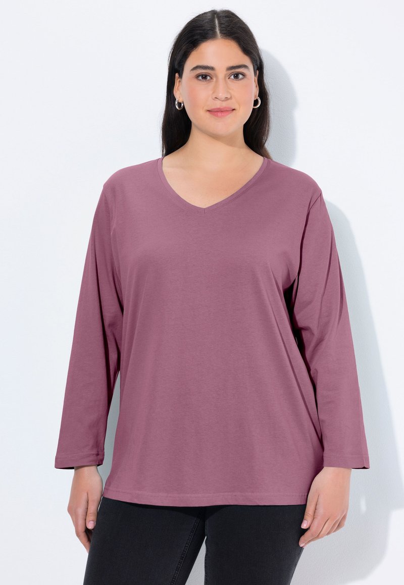 Długi rękaw, bluzka typu V-neck w kolorze mauve, ma luźny krój i miękki materiał. Rękawy są lekko zwężane przy mankietach, co dopełnia całość projektu.