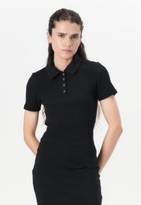 Black ribbed polo dress with short sleeves, featuring a buttoned placket and a fitted silhouette. The fabric has a smooth texture.