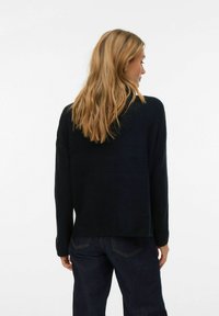 Tumši zils, adīts džemperis ar brīvu piegriezumu, ribotām apmalēm un piedurknēm. Mugura ir vienkārša, valkāts kopā ar tumšām džinsām.