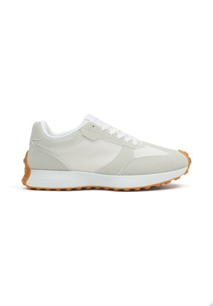 Zapatilla deportiva gris claro y blanca con cordones blancos, parte superior de malla y ante, entresuela blanca y suela exterior de goma con patrón de banda de rodadura.