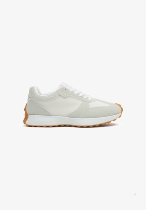 Zapatilla deportiva gris claro y blanca con cordones blancos, parte superior de malla y ante, entresuela blanca y suela exterior de goma con patrón de banda de rodadura.