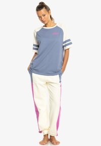 Modrá a krémová raglánová tričko s šedými pruhmi a logom "ROXY", v kombinácii s krémovými nohavicami s ružovými bočnými panelmi.