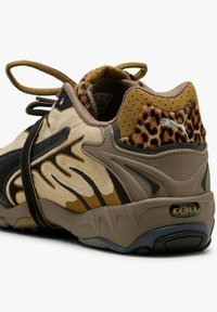 Sneaker con una combinazione di suede color cuoio e pelle nera, caratterizzata da un accento con stampa leopardata, suola in gomma e un prominente logo "CELL" sul tallone.