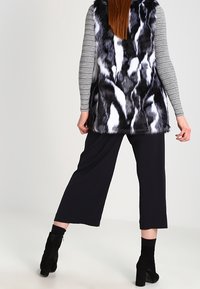 Kamizelka z sztucznego futra w czarno-białe wzory zwierzęce, nałożona na paskowaną bluzkę z długim rękawem. Połączona z czarnymi spodniami o szerokich nogawkach i botkami za kostkę.