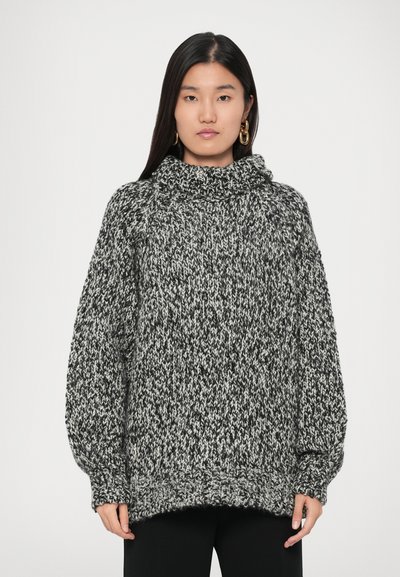 Pull en tricot épais noir et blanc, avec un col haut, des épaules tombantes et un ourlet côtelé. Tissu texturé et chaud.