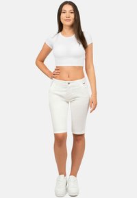 Bermudas blanches en denim avec un design classique à cinq poches, coupe droite et une texture légèrement extensible. Associées à un haut court blanc ajusté.