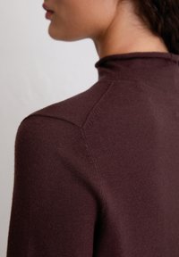 Bordeaux trui met een hoge hals, voorzien van een zachte textuur en subtiele stiksels langs de schouders en achterkant.