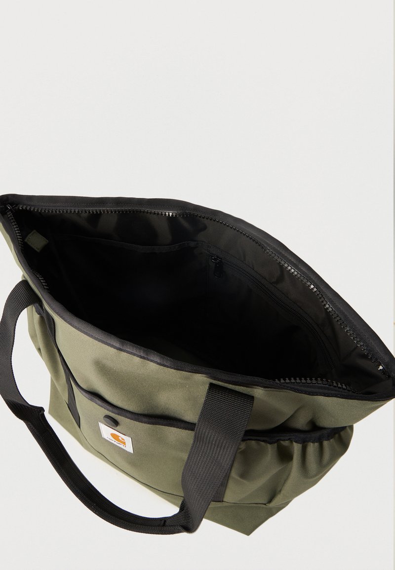 Bolsa tote verde oliva con asas negras, cremallera superior abierta, bolsillo delantero con botón a presión y amplio interior negro con compartimento con cremallera.