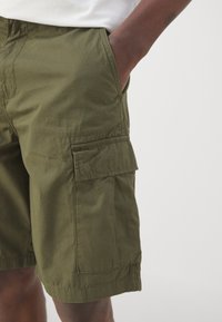 Pantalones cortos de carga de color verde oliva con un bolsillo lateral, cinturilla elástica y tela de algodón duradera, diseñados para confort y utilidad.