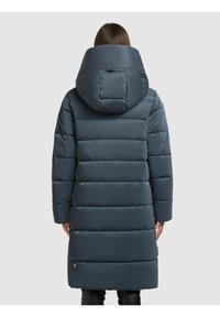 Tamsiai mėlynas paminkštintas paltas su dideliu kapišonu, horizontaliomis siūlių linijomis, ilgomis rankovėmis ir šoninėmis kišenėmis, pagamintas iš lygaus, atsparaus vandeniui audinio.