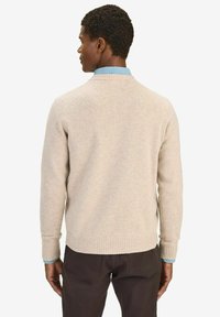 Beige gebreide trui met geribde zoom en manchetten, met een ronde hals. Draagt over een lichtblauw overhemd met kraag en gecombineerd met donkere trousers.