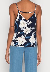 Camisole floreale navy con spalline sottili e design a V sul retro. Presenta grandi fiori bianchi e foglie verdi, realizzata in tessuto leggero.