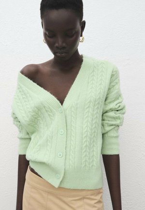 Chaqueta de punto con cable en verde claro, con escote en V profundo, mangas oversize y tres botones. Textura suave con un ajuste relajado.