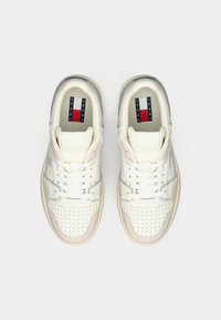 Pair of white and beige Tommy Jeans sneakers with white laces, perforated toe area, and branded insoles, viewed from above on a white background.