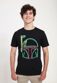 Czarna koszulka z żywą neonową grafiką hełmu w zielonym i czerwonym kolorze, z dekoracyjną nutą muzyczną w żółtym. Gładka tekstura, casualowy krój.