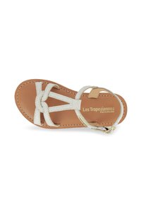 Sandal de cuero blanco con un diseño de tira en T, correas texturizadas y una plantilla color marrón con branding en relieve. Acento de hebilla en tono dorado en la correa del tobillo.