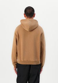 Brown hooded sweatshirt with a textured finish, cropped design, and a ribbed hem. Features a simple, unobtrusive style.