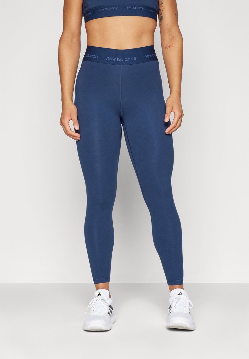 Leggings deportivos de color azul marino con una cinturilla gruesa, textura suave y detalle de logotipo. Combinados con zapatillas blancas.