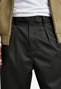 Pantalon noir avec une texture lisse, doté de plis avant, d'une coupe droite et d'une taille discrète avec une fermeture à bouton. Assorti à un hoodie zippé kaki.