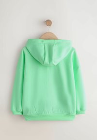 Sweat à capuche vert menthe avec cordon de serrage, tissu doux, manches longues et poignets côtelés. Suspendu sur un cintre en bois contre un fond clair.