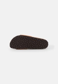 Suela de goma marrón con un patrón de olas texturizado, con un material superior en color marrón anaranjado, ligeramente acolchado y con diseño de punta redondeada.